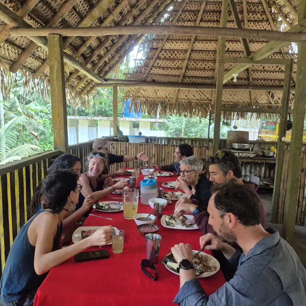 Todos comiendo juntos en la mesa larga roja bajo el techo de paja