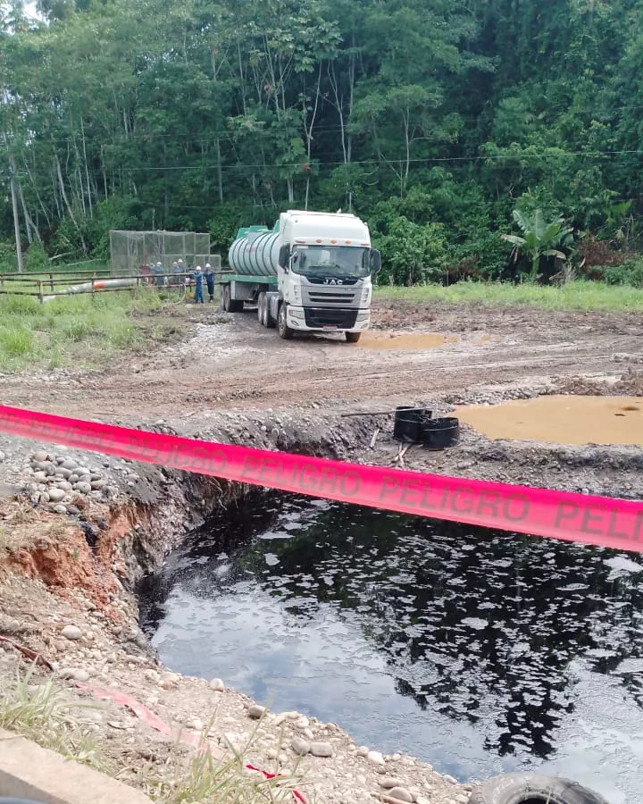 Piscina de crudo acordonada con cinta de peligro junto a un tanquero en un campo petrolero